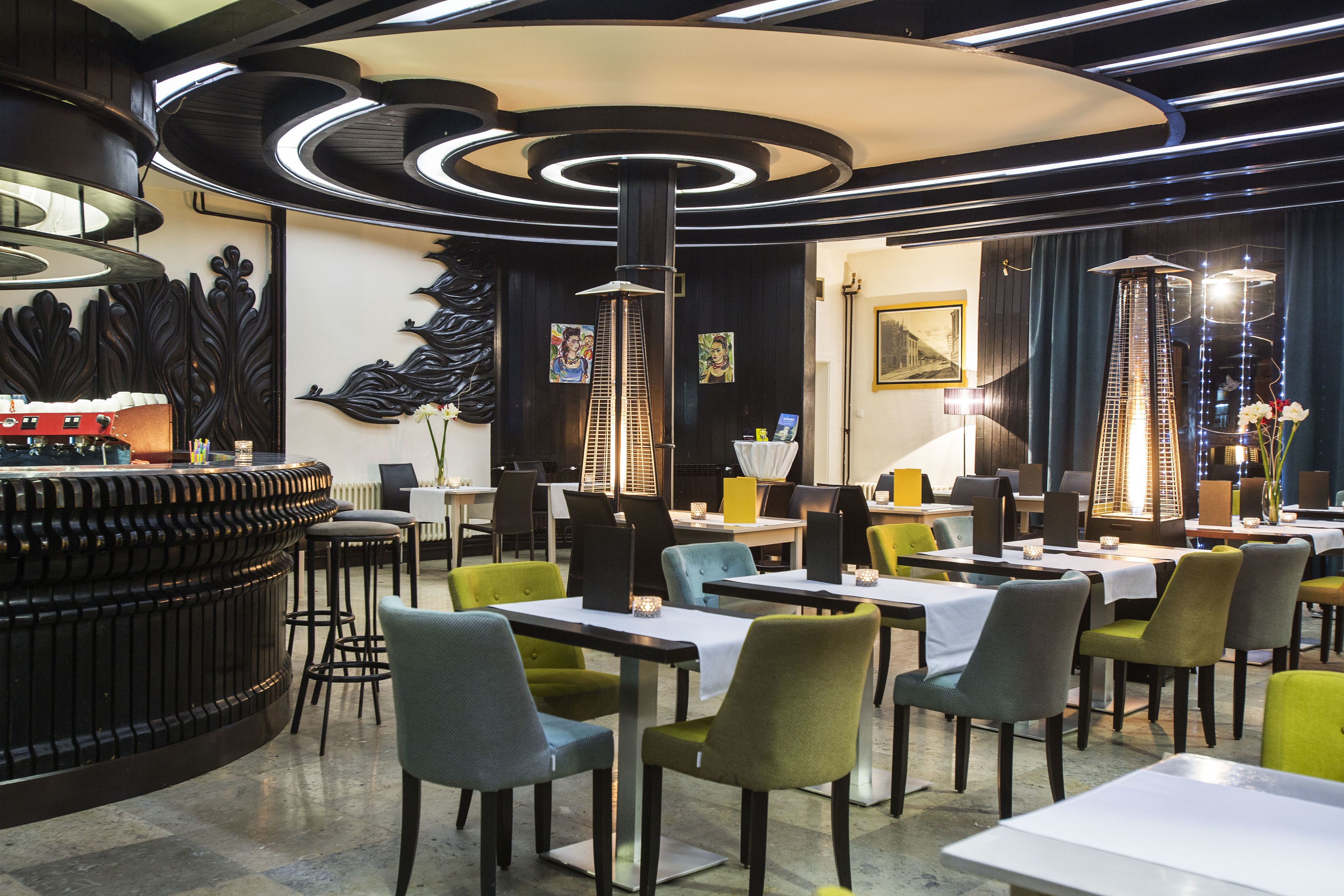 A modern restaurant interior with a central bar, multiple dining tables, and chairs.