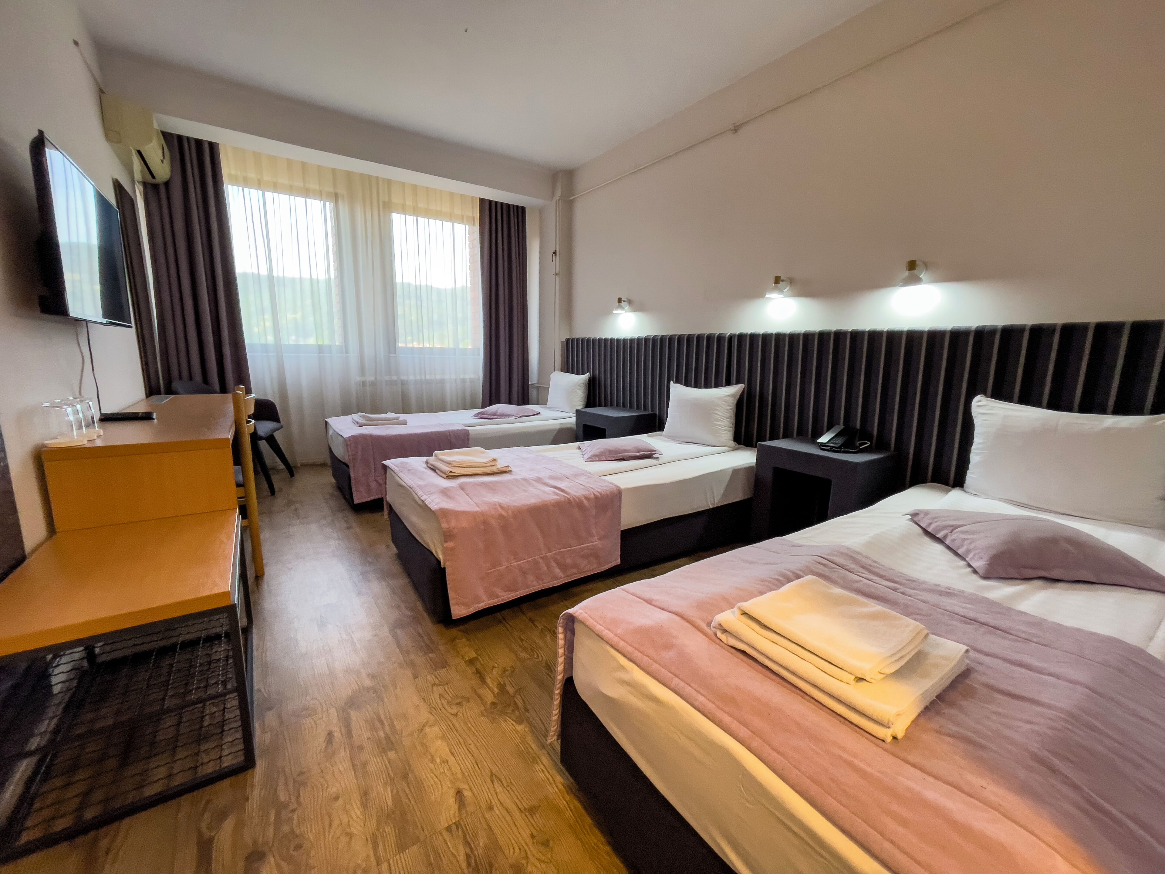 Habitación de hotel con dos camas individuales, un escritorio, una silla, un televisor y una ventana con cortinas.