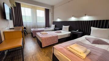 Habitación de hotel con dos camas individuales, un escritorio, una silla, un televisor y una ventana con cortinas.