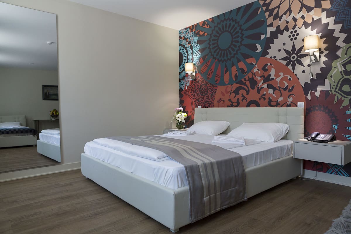 Une chambre d’hôtel moderne, dotée d’un grand lit, de tables de chevet et d’une fresque murale décorative.