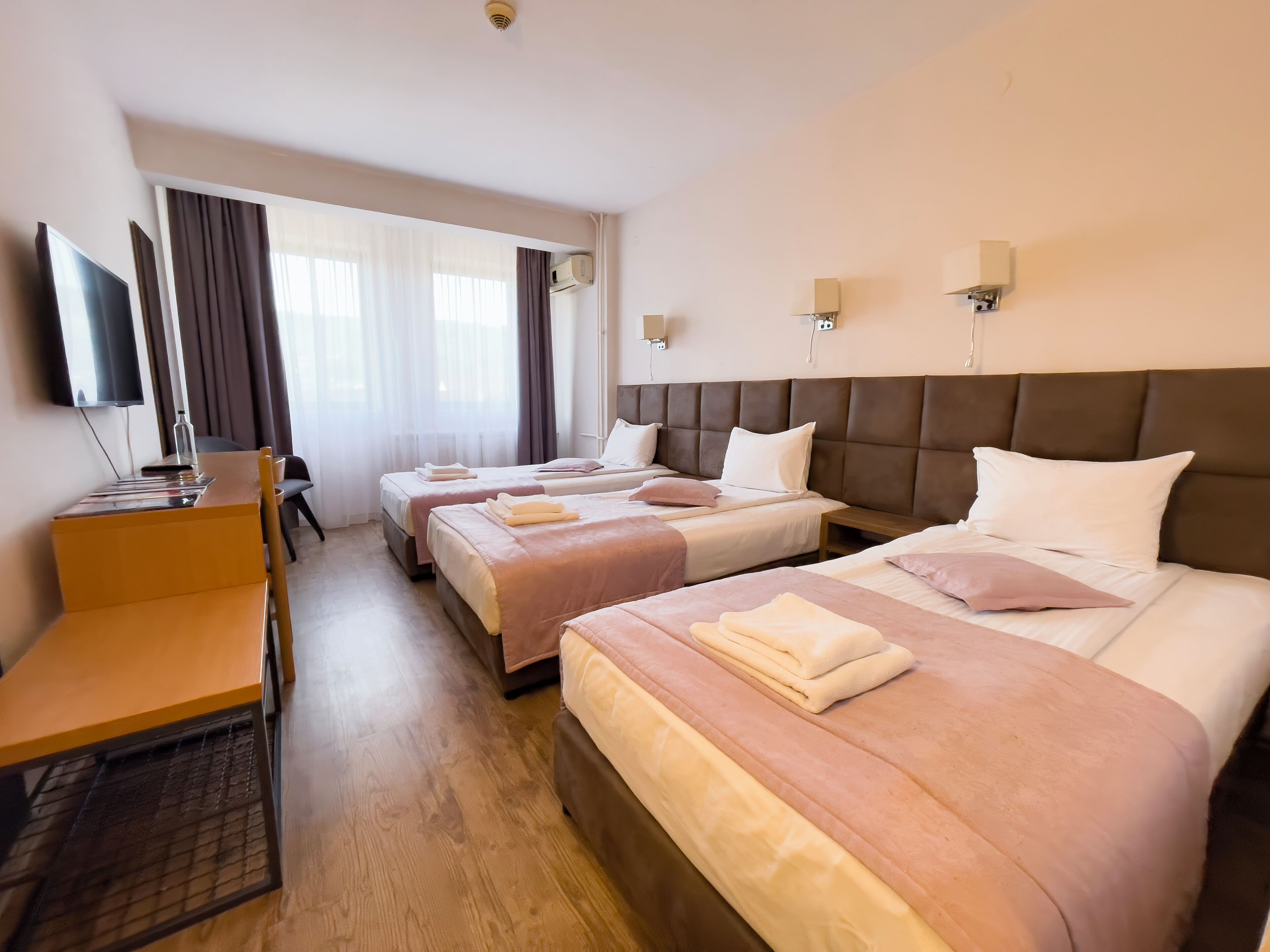 Une chambre d’hôtel avec trois lits, un bureau, une télévision et une fenêtre avec des rideaux.