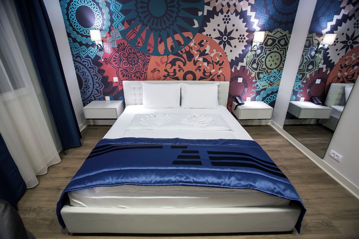 Quarto de hotel com cama, duas mesas de cabeceira e uma parede com padrões elaborados.