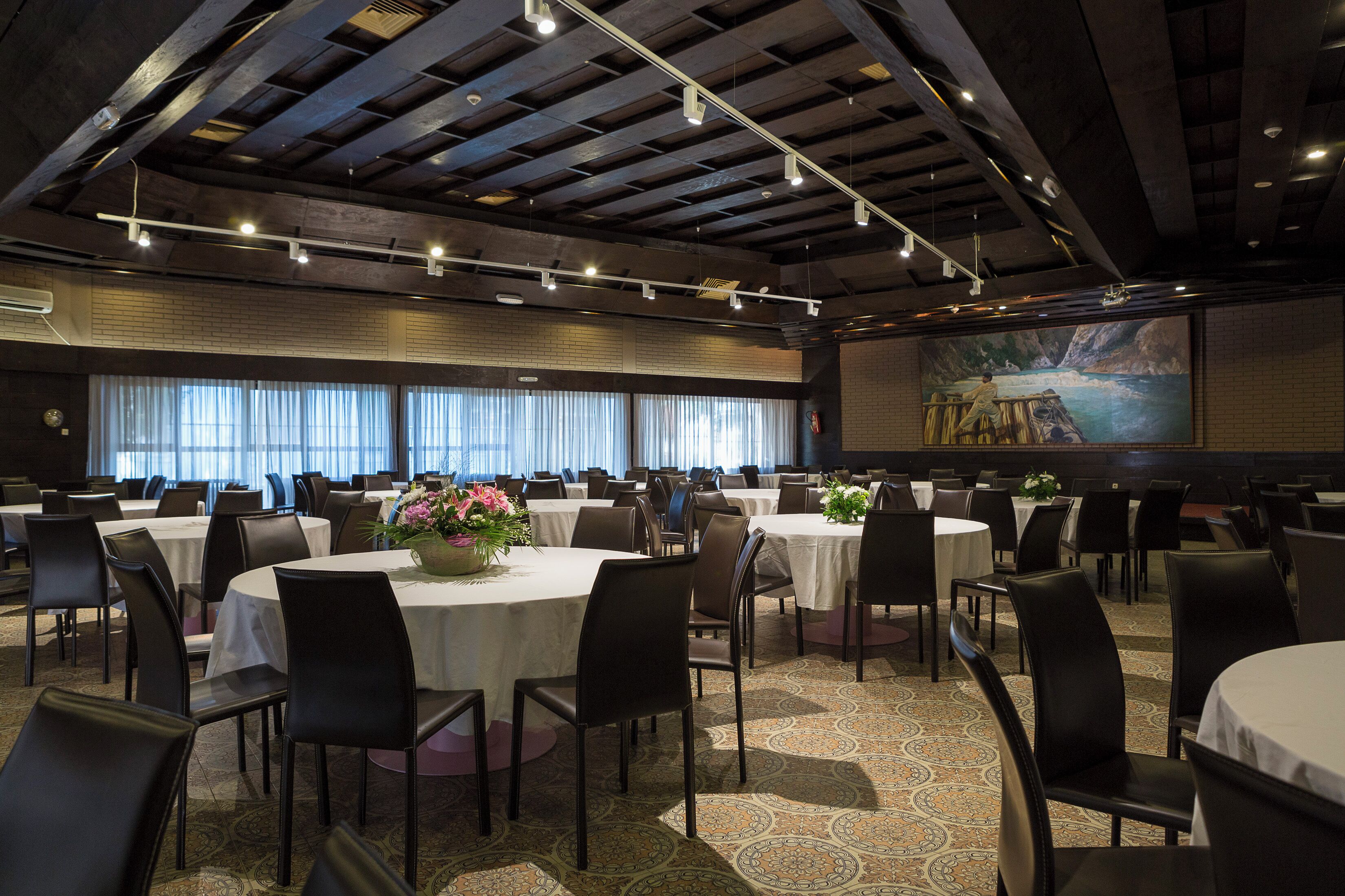A banquet hall with round tables, black chairs, and a large screen displaying a scenic image.