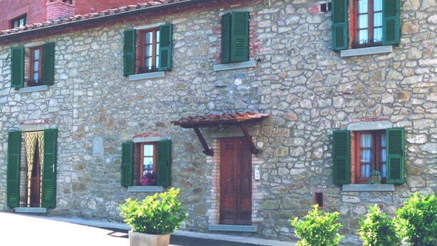 Un edificio de piedra con contraventanas verdes, una puerta de madera y plantas en macetas al frente.