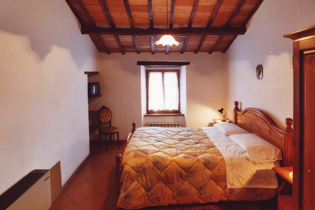 A bedroom with a wooden bed, a window with curtains, a chair, and a radiator.
