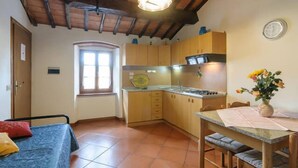 Una cocina compacta con armarios de madera, una mesa de comedor con sillas acolchadas, un ventanal pequeño y un reloj en la pared.