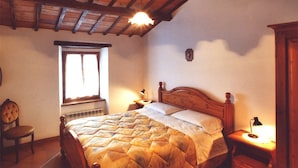 Un dormitorio con cama de madera, una ventana, una silla y una mesita de noche con lámpara.