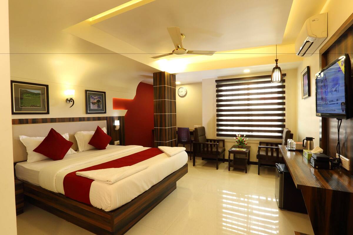 A hotel room with a bed, a desk, a chair, a TV, and a window with blinds.