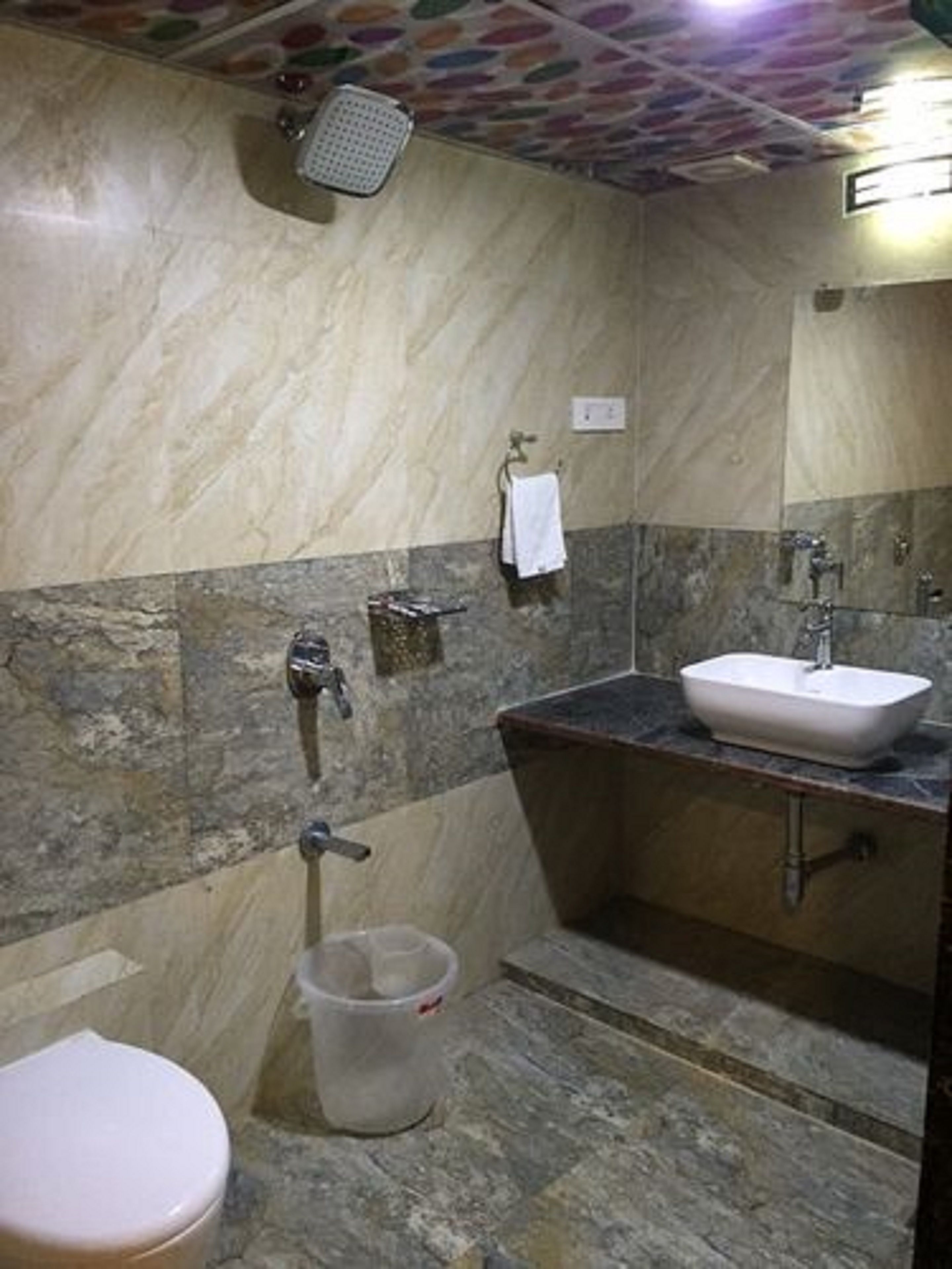 A bathroom with a toilet, a sink, a shower, and a trash bin.