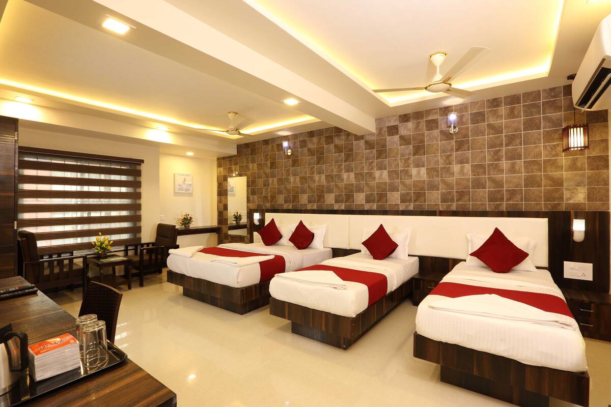 A hotel room with three beds, a desk, chairs, and a ceiling fan.