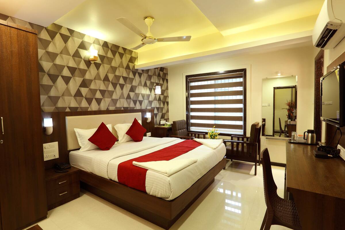 A modern hotel room with a large bed, a desk, and a wardrobe.