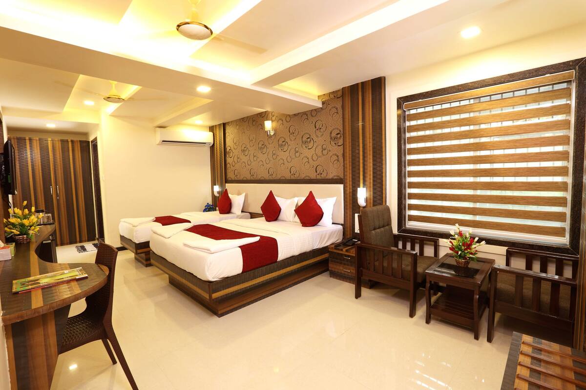 A hotel room with a large bed, a desk with a chair, a small table with a chair, and a large window with blinds.