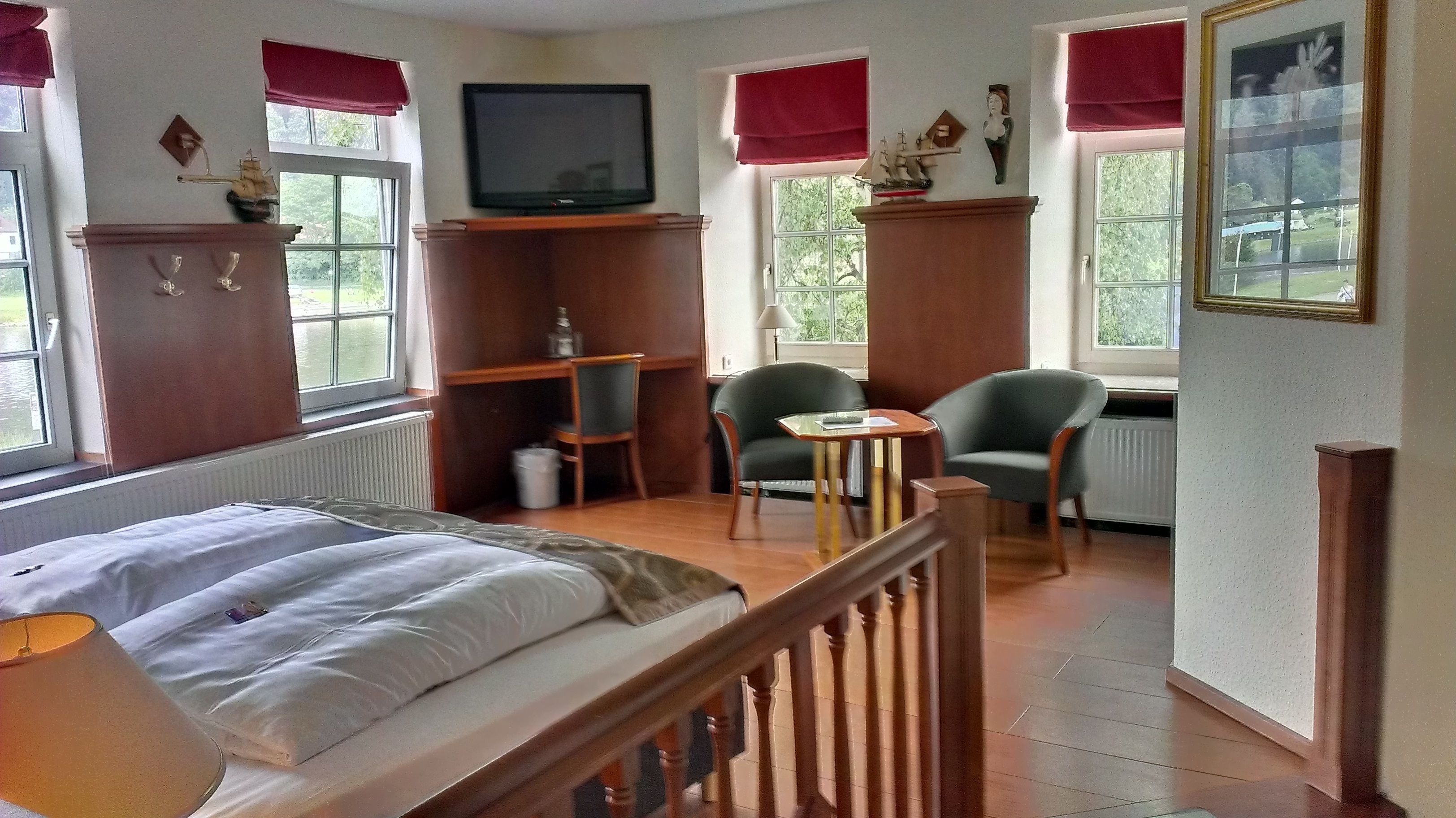 Habitación de hotel con cama, dos sillas, una mesita, televisor y ventana con vistas a zonas verdes.