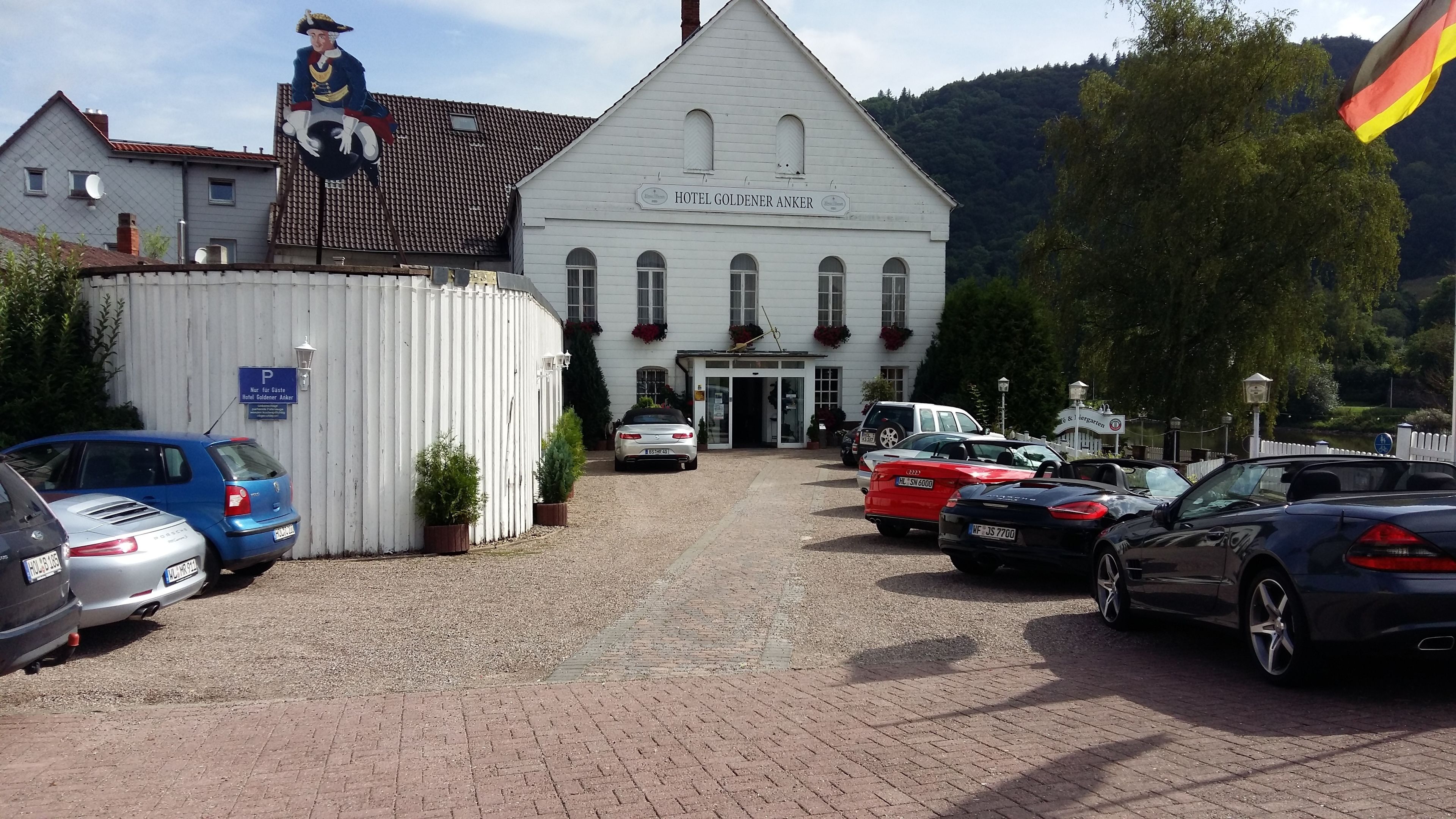 A white building with a sign reading "HOTEL GOLDENER ANKER" and a flag.