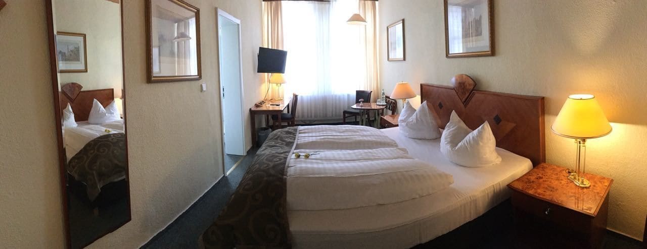 Una habitación de hotel con una cama grande, un escritorio con silla, un televisor y una lámpara.