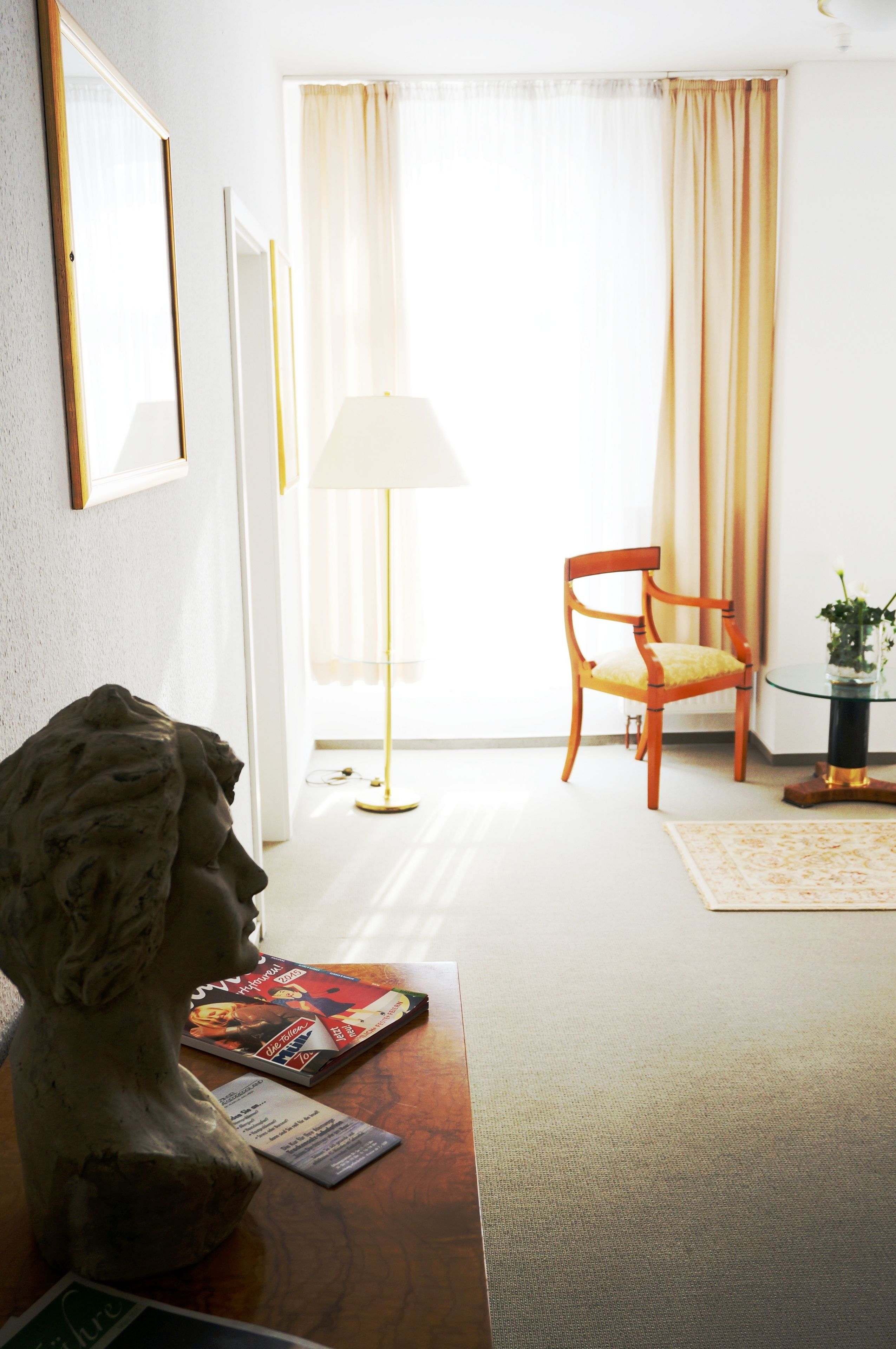 A room with a wooden chair, a lamp, a statue, and a table with a magazine.