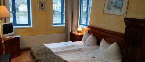 A hotel room with a bed, a TV, a lamp, and two windows.