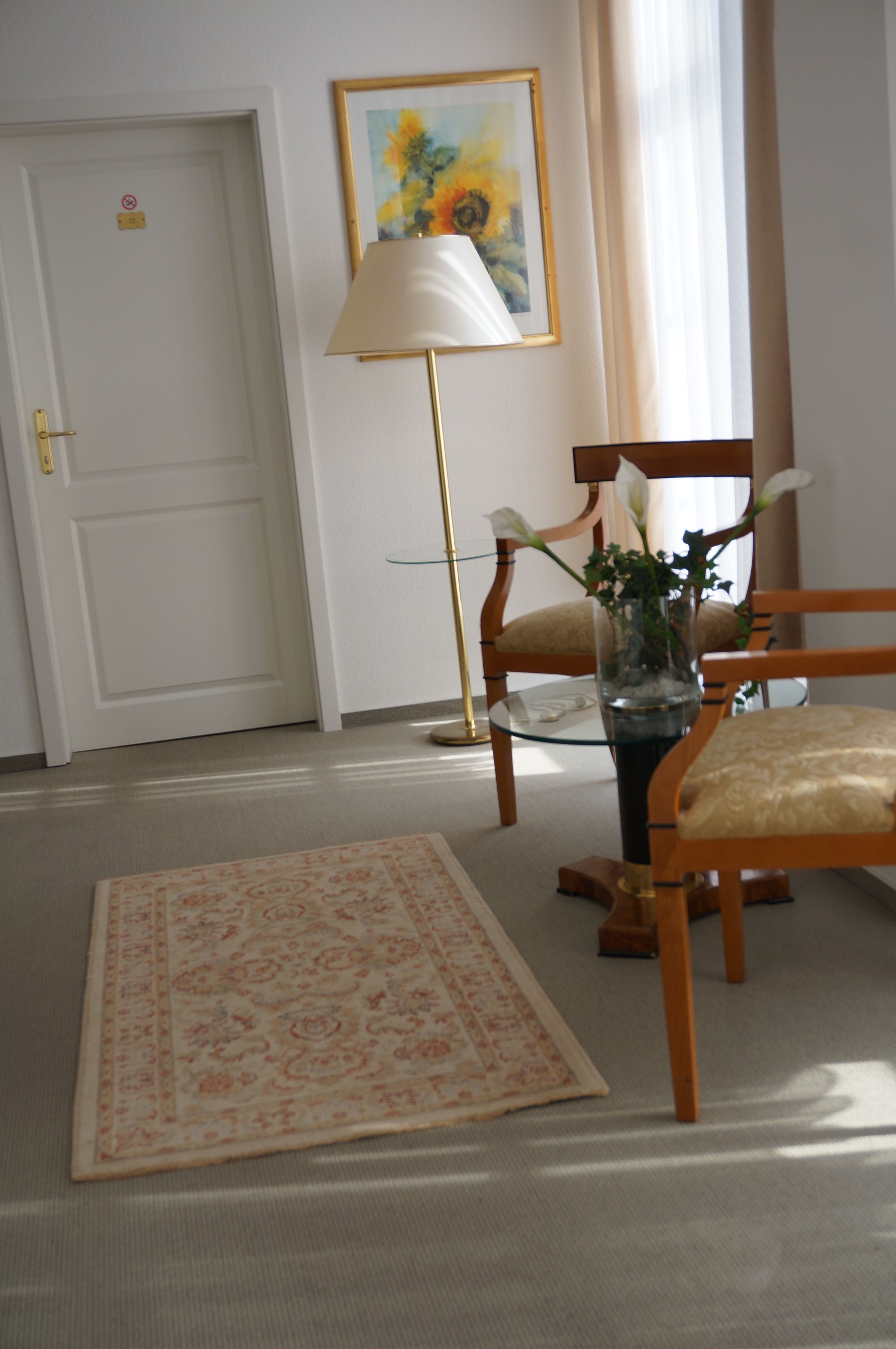 Una habitación con una silla de madera, una mesa de vidrio con un florero, una lámpara de pie y una puerta con un letrero de 'prohibido el acceso'.