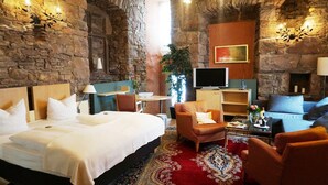 A hotel room with a stone wall, a bed, a sofa, a TV, and a fireplace. - Goldener Anker (Bodenwerder)