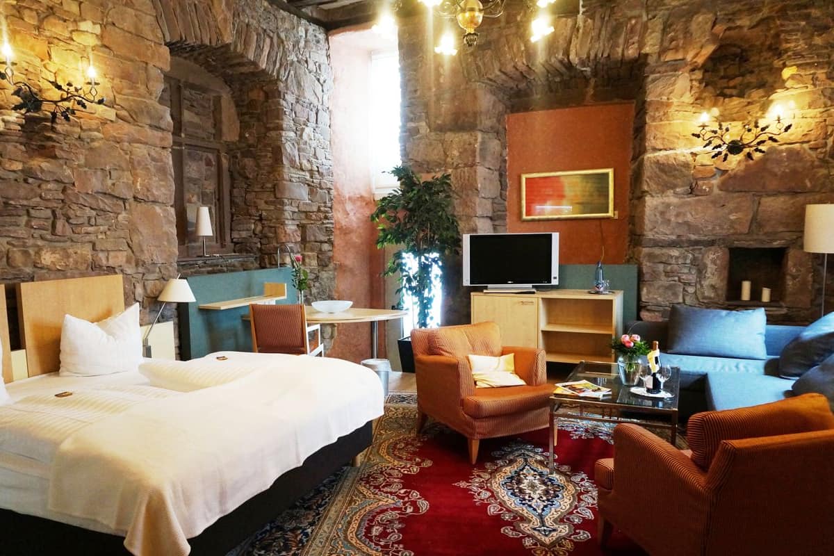 A hotel room with a stone wall, a bed, a sofa, a TV, and a fireplace.