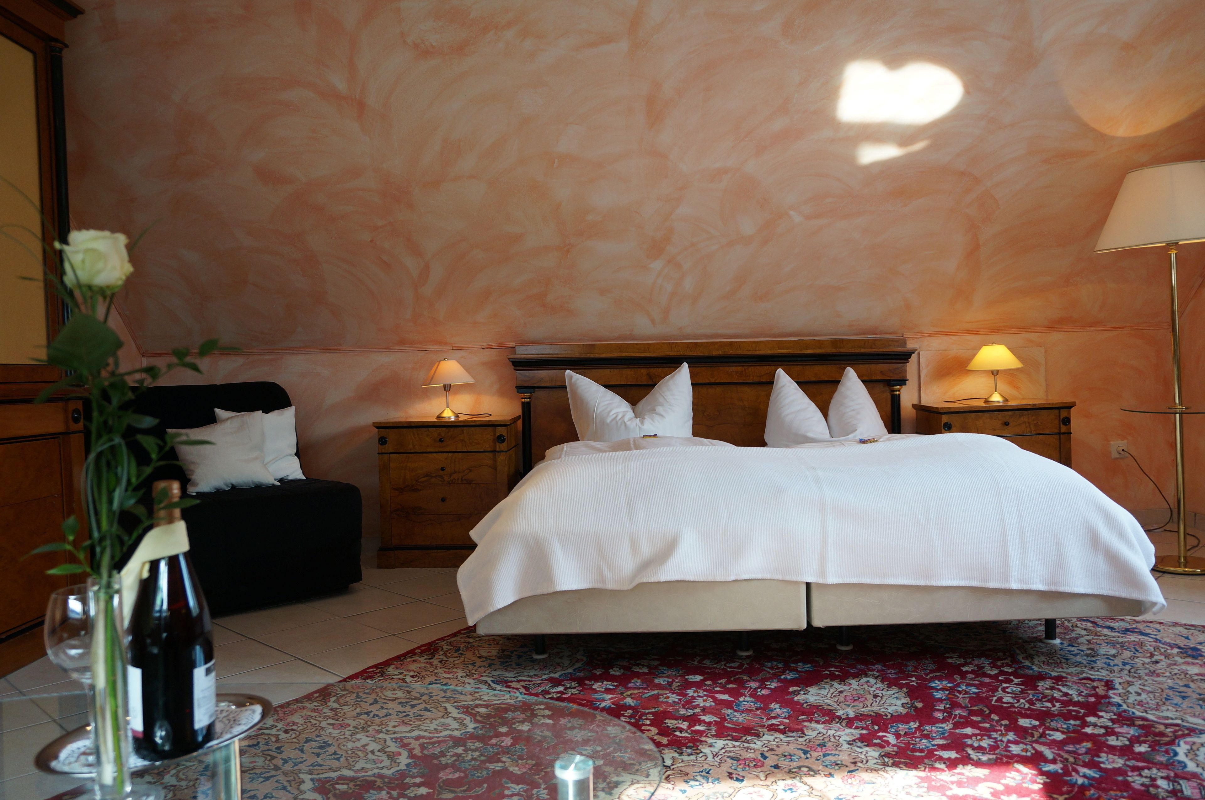 A bedroom with a large bed, two bedside tables with lamps, a red floral rug, and a wall with a heart-shaped design.