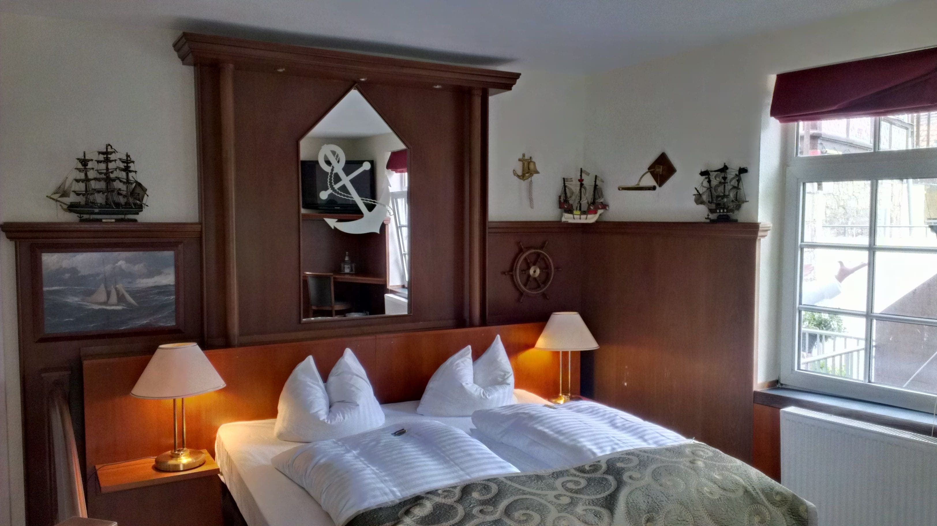 A hotel room with a large bed, two bedside lamps, a ship's wheel, and nautical decorations.