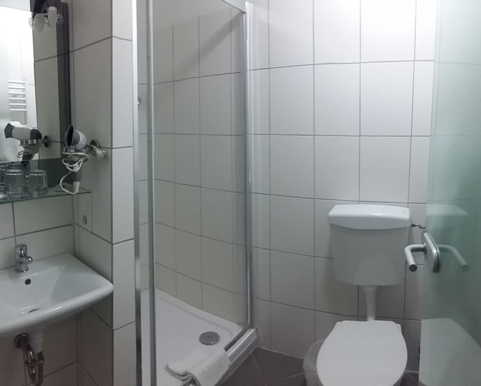 Ein Badezimmer mit Duschkabine aus Glas, einer weißen Toilette und einem Waschbecken mit Spiegel darüber.