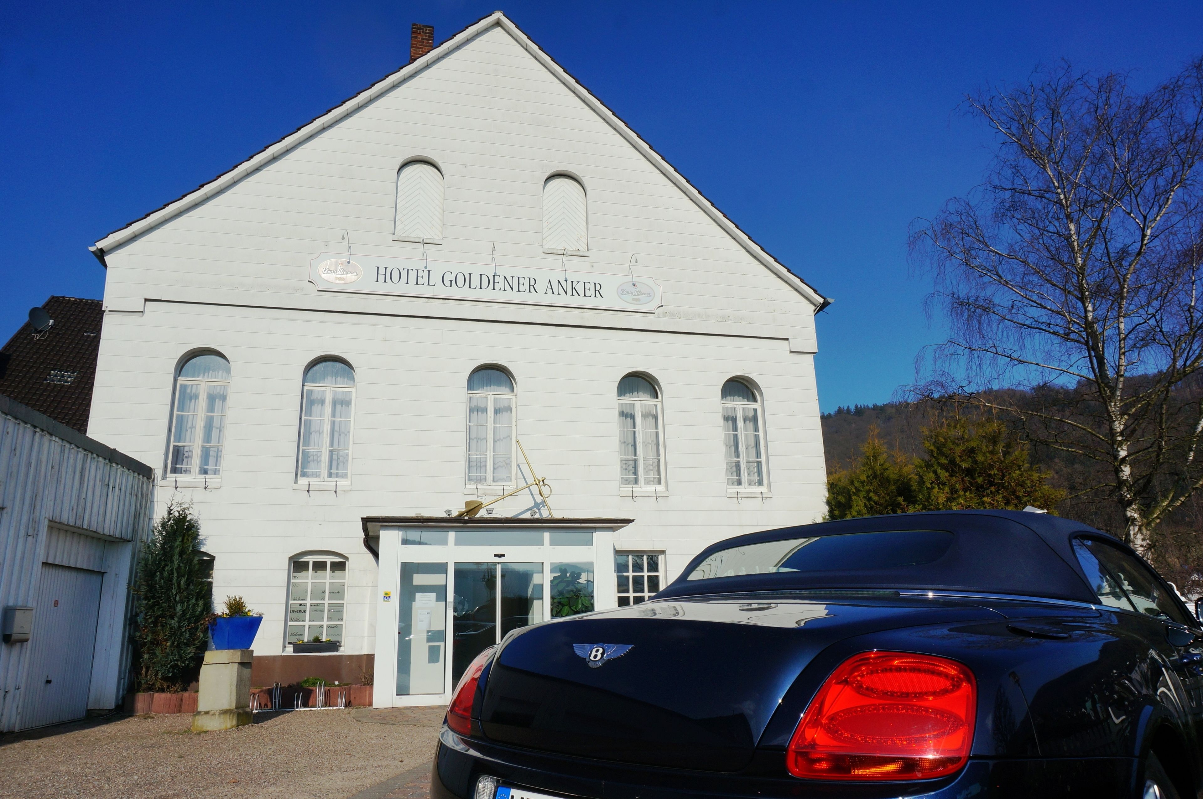 A white building with the sign "HOTEL GOLDENER ANKER" and a parked black car in front.