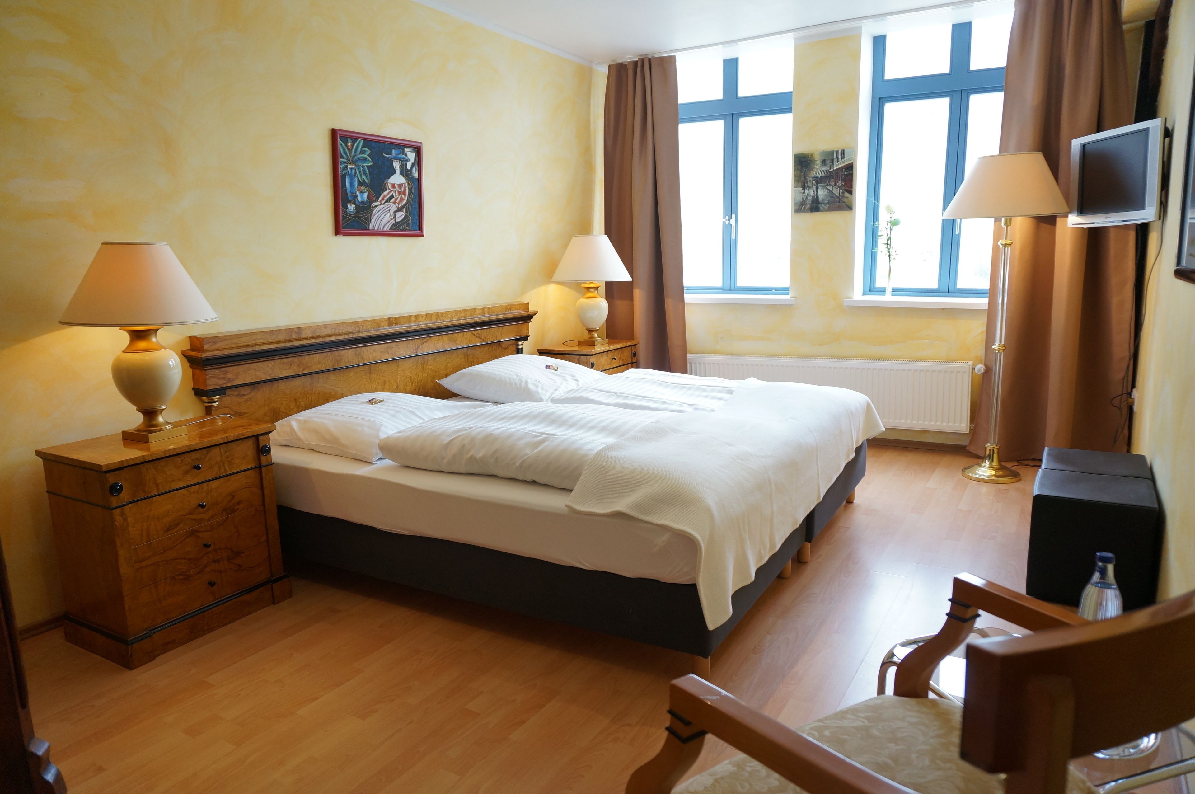 A hotel room with a bed, two bedside tables with lamps, a television, and a window with curtains.