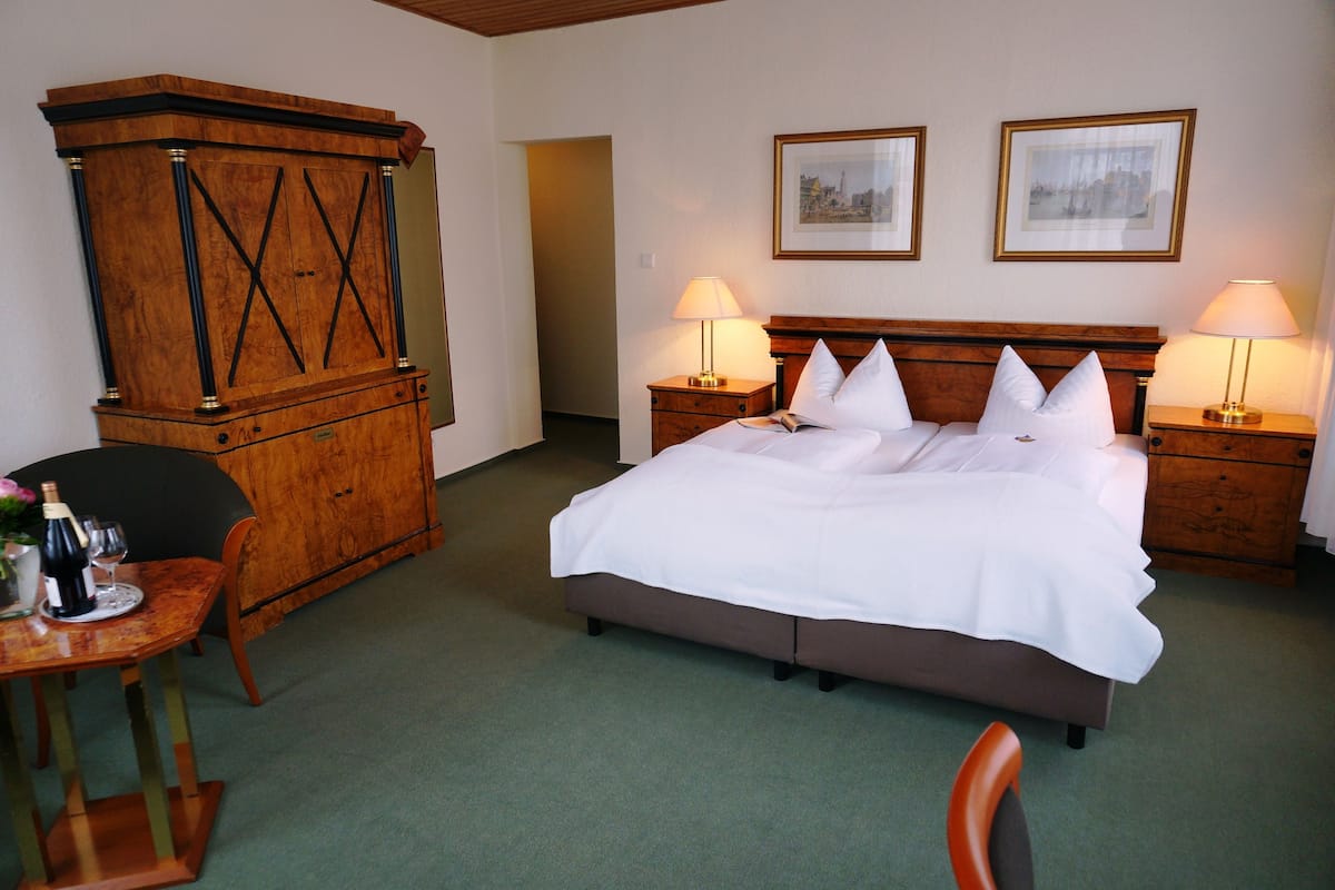 A hotel room with a large bed, two bedside tables with lamps, a wooden cabinet, and two framed pictures on the wall.