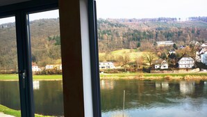 A view through a window of a lake with houses and a forested hill in the background. - Goldener Anker (Bodenwerder)