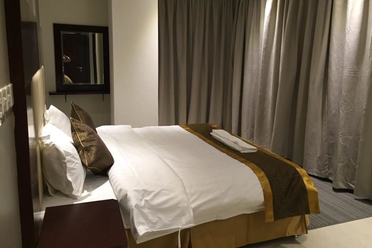Une chambre d’hôtel avec un lit bien fait, une table de chevet, un miroir et une vue sur les rideaux de l’extérieur.