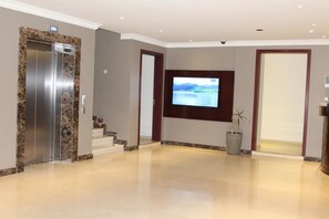 Un hall d’entrée moderne avec un ascenseur en marbre, un téléviseur à écran plat fixé au mur et une plante en pot.