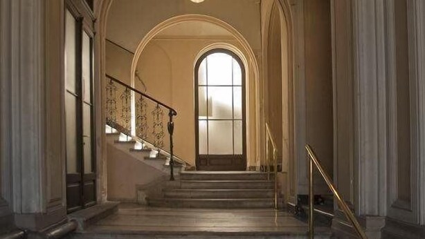 A grand staircase with a high ceiling and arched architecture, leading to a landing with a large window. - House5 (Trieste)