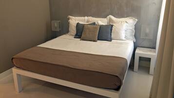 Un lit avec une couvre-lit marron et des oreillers blancs, une table de chevet et un luminaire fixé au mur.