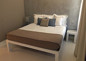 A bed with a brown bedspread and white pillows, a bedside table, and a wall-mounted light fixture. - House5 (Trieste)