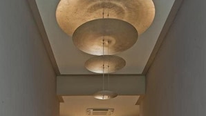A hallway with a polished floor, a ceiling with circular light fixtures, and a door leading to a room with a fireplace. - House5 (Trieste)