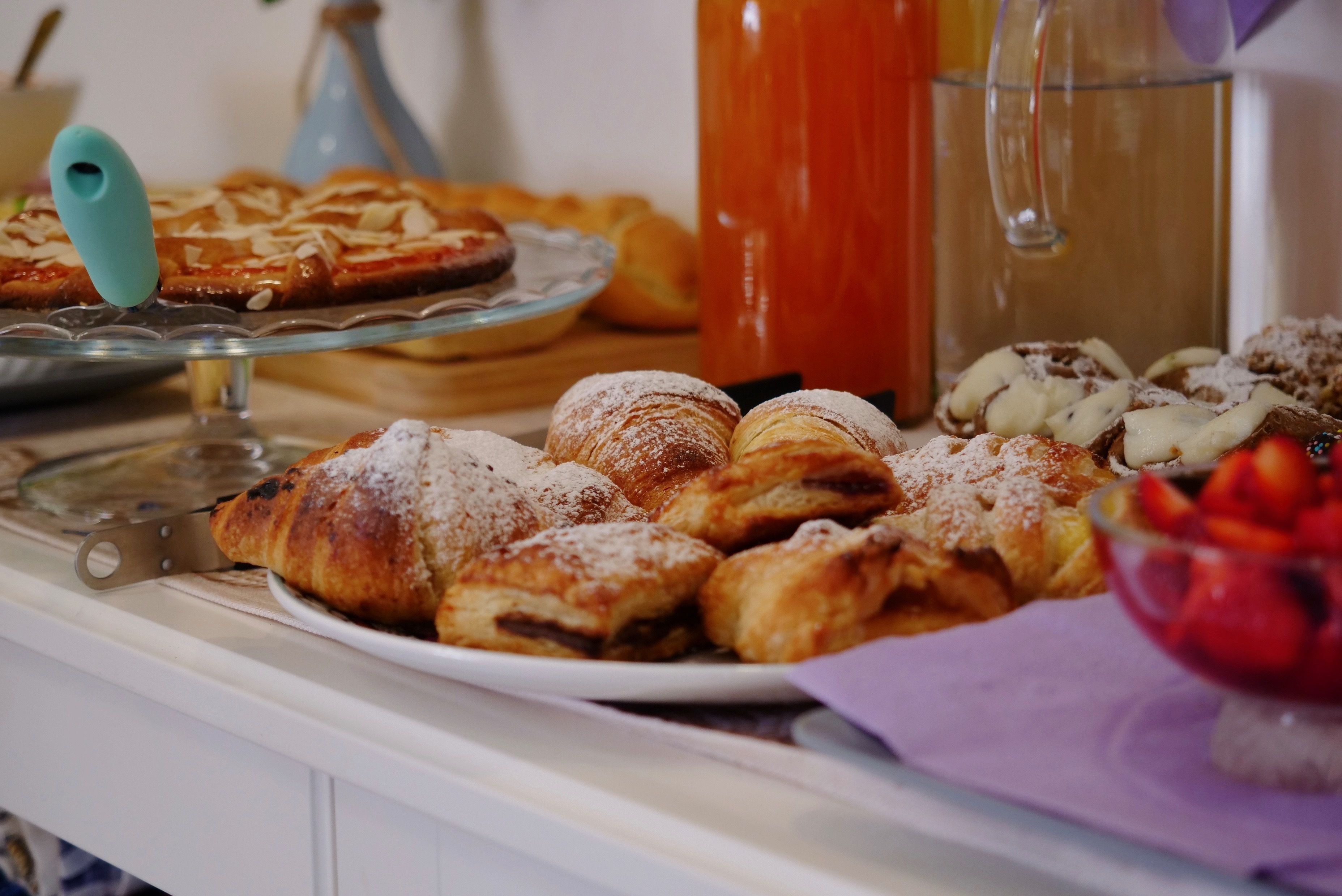 Un bufé con diversas pastas y postres, incluyendo cruasanes y un cuenco de fruta.