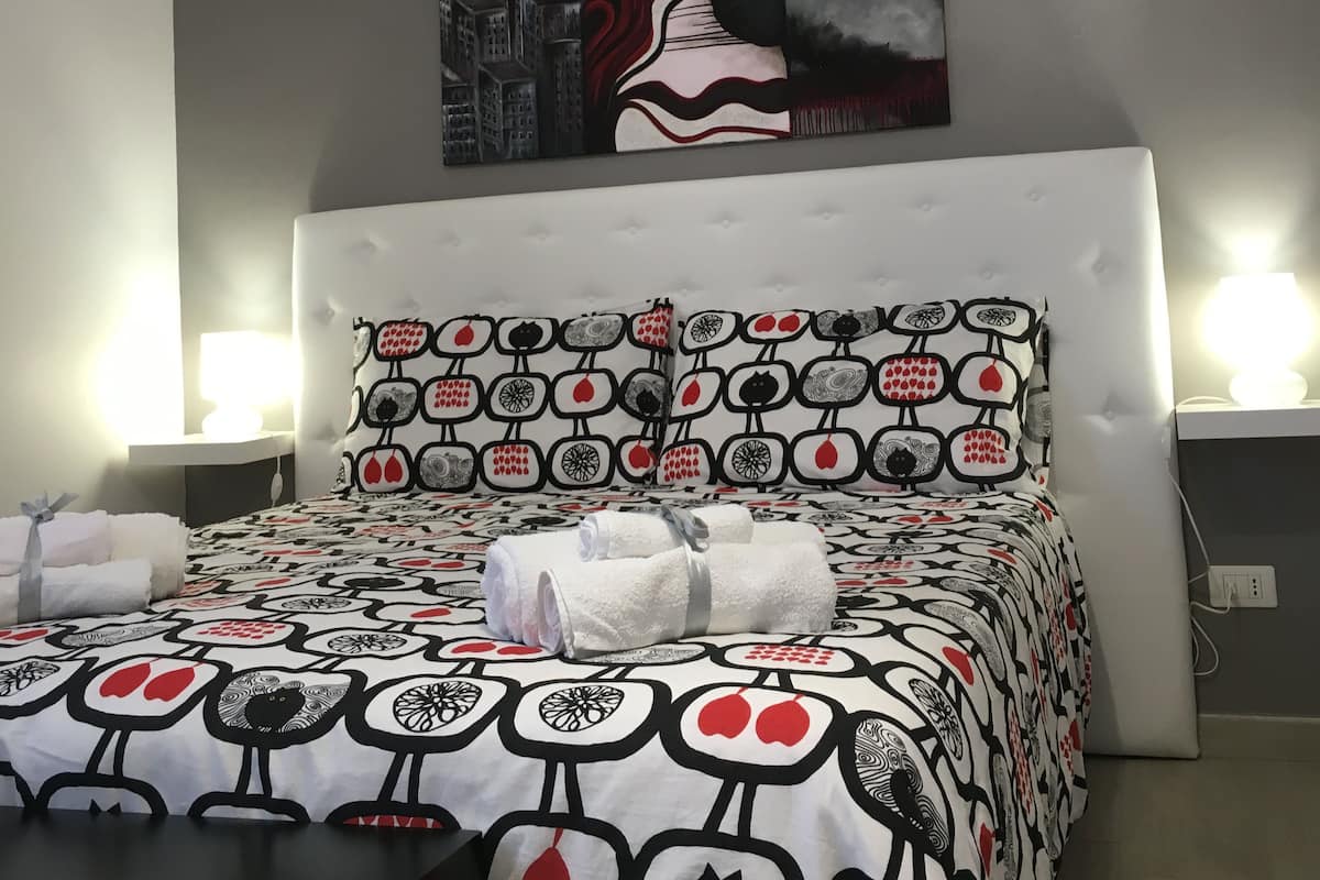 A hotel room with a bed featuring a patterned bedspread, a headboard with a unique design, and a large abstract painting on the wall.