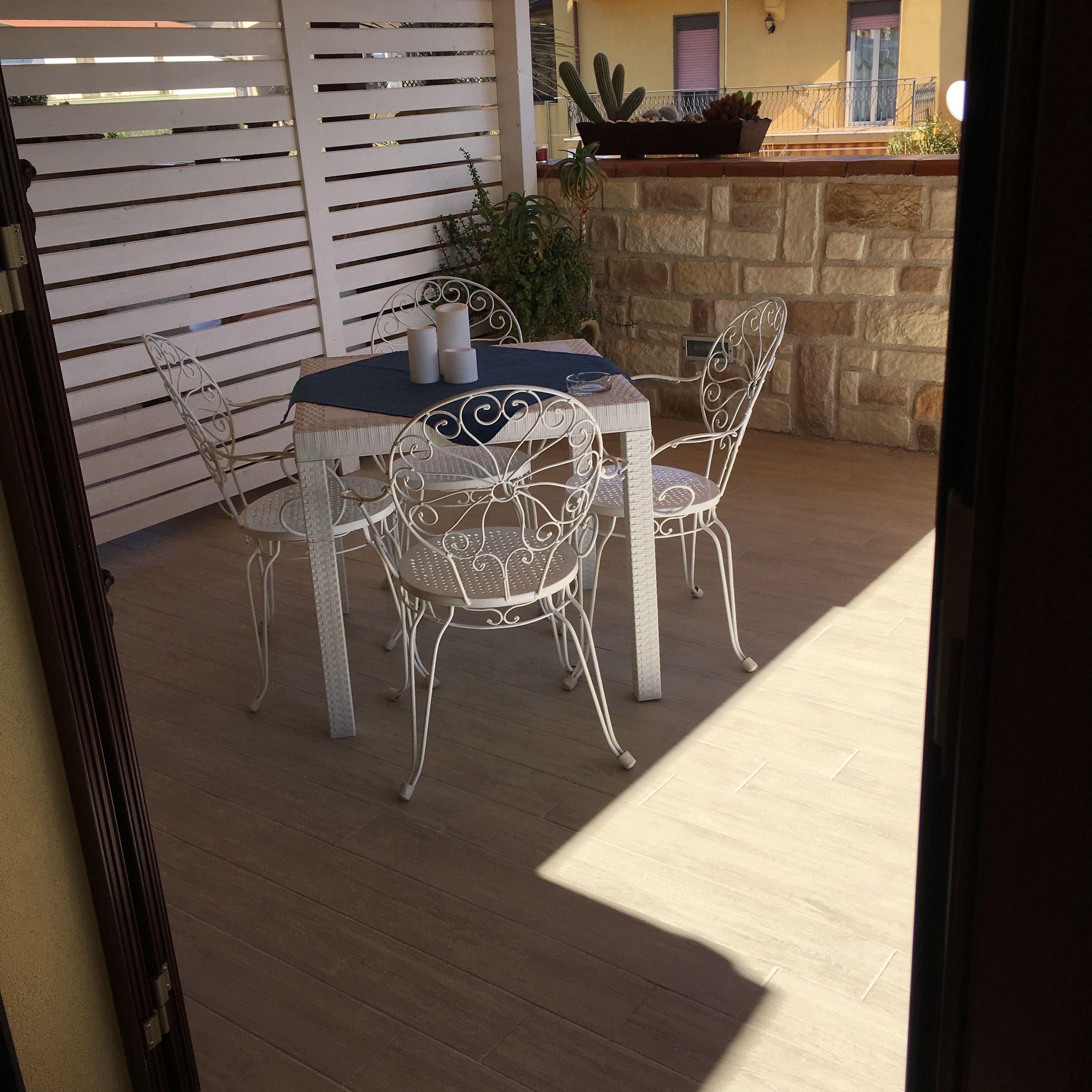 An outdoor patio with a round table and four chairs, a white metal fence, and a stone wall with a cactus planter.