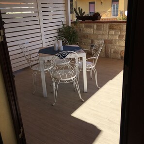An outdoor patio with a round table and four chairs, a white metal fence, and a stone wall with a cactus planter. - Templi e Arte (Agrigento)
