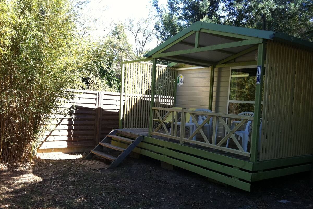 Een klein, gelijkvloers vakantiehuisje met een houten terras en een hellingbaan naar de ingang.