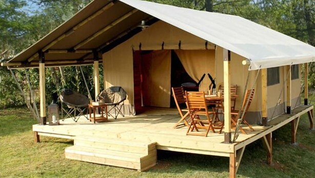 Una carpa con un porche cubierto, sillas de madera, una mesa y una parrilla.