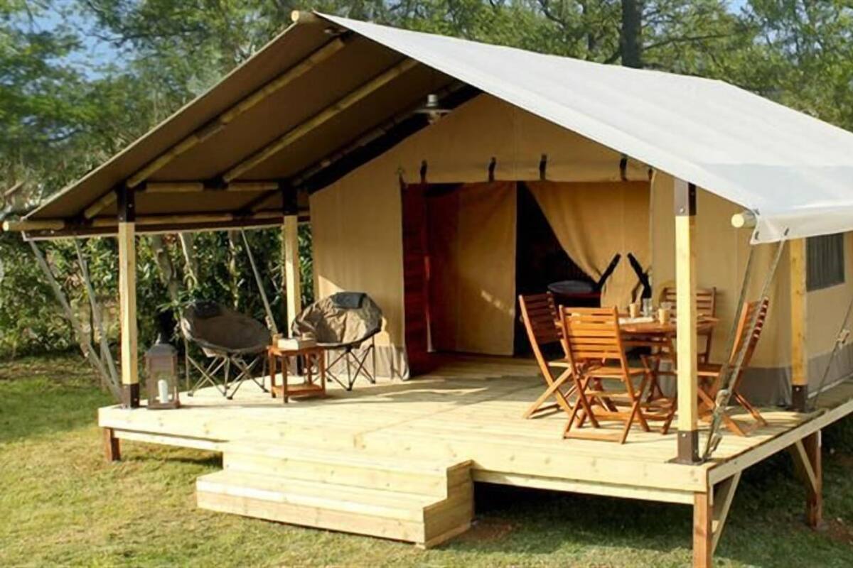 Een tent met een overdekte veranda, houten stoelen, een tafel en een barbecue.