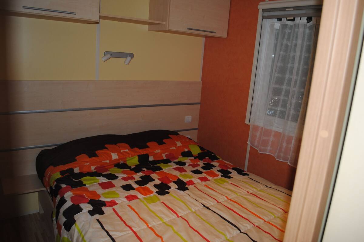 Een slaapkamer met een bed, een raam met gordijn en een houten garderobe.