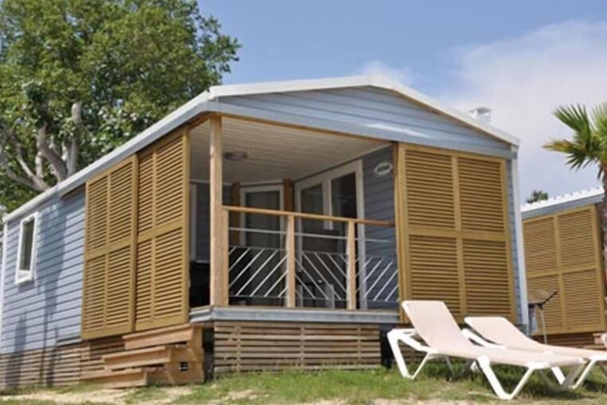 Een klein, laag huis met een veranda en twee schuifdeuren.