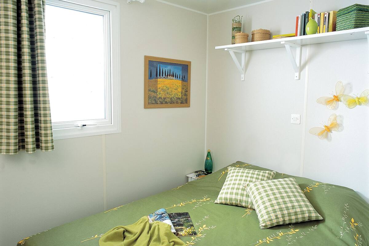 Een slaapkamer met een bed, een raam met gordijnen, een schilderij, een plank met boeken en manden, en een muur versierd met vlinderstickers.
