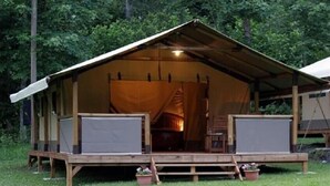 Una cabaña rústica con terraza de madera, un porche cubierto y una chimenea central.