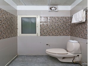 A bathroom with a toilet, a window, and patterned tiles on the walls.