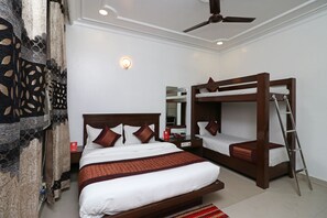 A hotel room with a large bed, a smaller bunk bed, a ceiling fan, and a nightstand with a lamp.